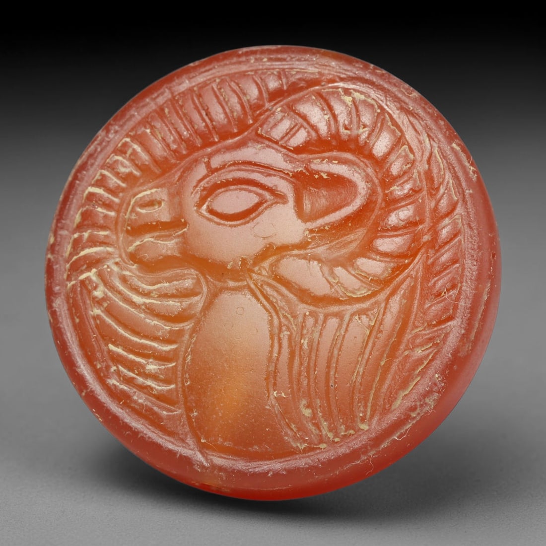 Ancient Medieval Early Islamic Period Carnelian Cameo Bead (c.7th-11th Century CE), 76EC: This circular pierced bead is crafted from natural carnelian, decorated with a finely executed cameo depiction of a winged ram, a meaningful talismanic symbol widely utilised within medieval Near East