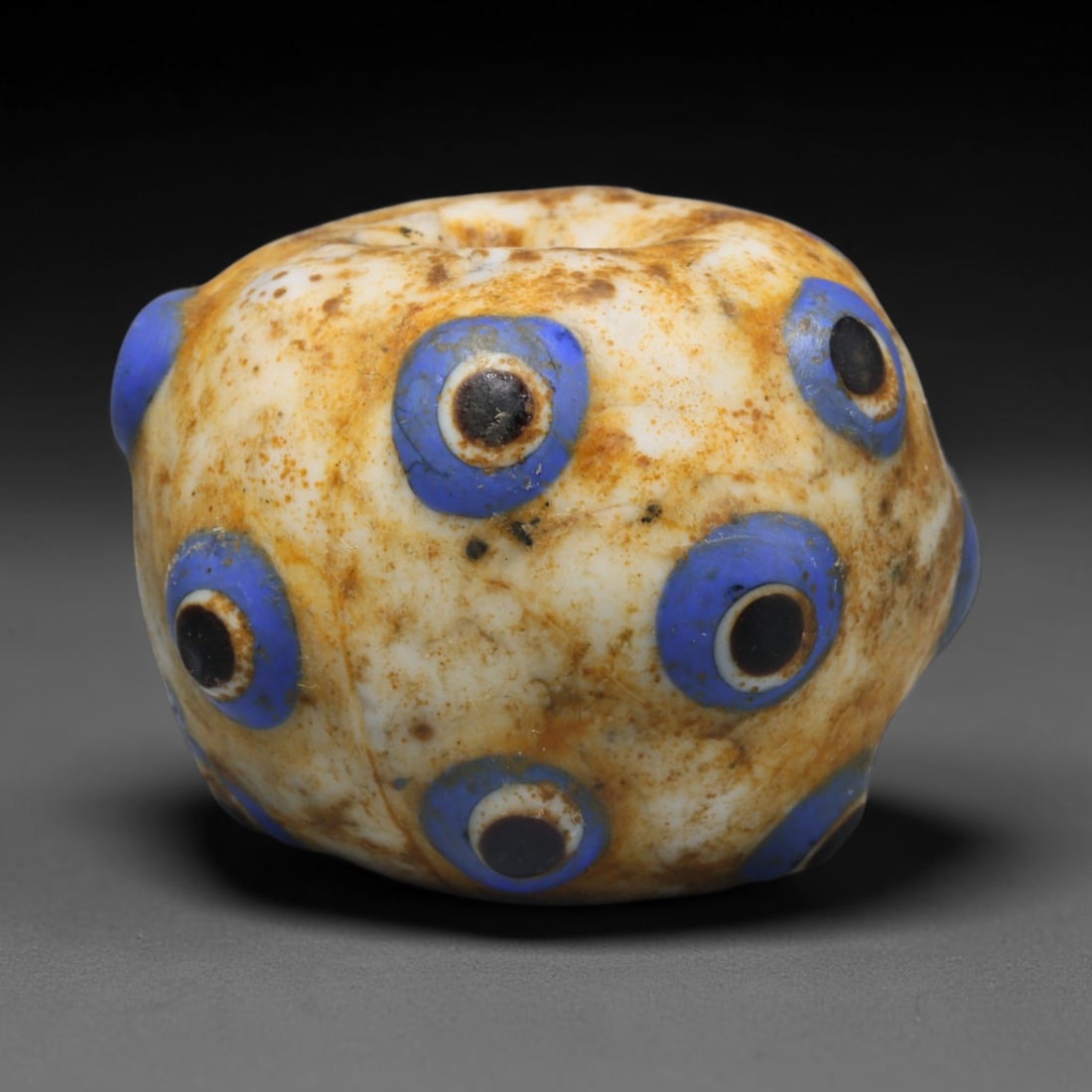 Ancient Medieval Islamic Eye Mosaic Glass Bead (800-1200 CE), 59ED: This antique mosaic glass bead originates from medieval Islamic glassmaking traditions, valued for personal adornment and protective talismanic wear. The creamy white glass base is adorned with multip