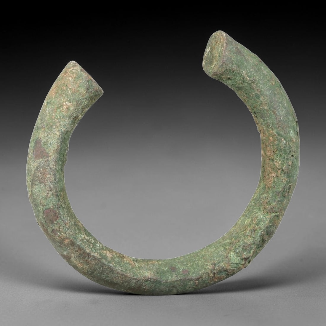 Ancient Roman Bronze Bracelet - Open Bangle Form, 34BN: Crafted from bronze, this open bracelet is formed as a thick, rounded rod creating a horseshoe-shaped cuff with a narrow gap between the flat terminals. The surface displays a heavily textured, uneven