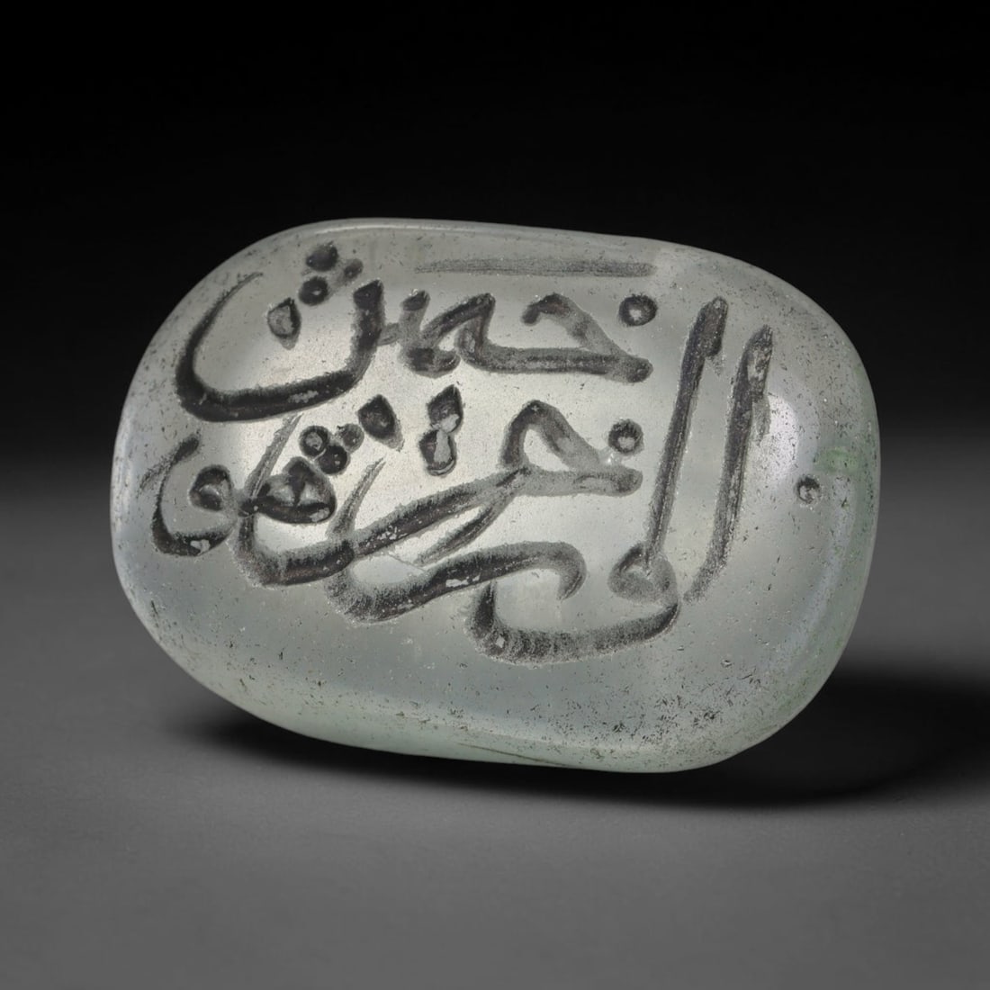 Early Vintage Islamic White Glass Calligraphic Intaglio Seal Cabochon (Post 1900 CE), 82BX: This early vintage glass intaglio seal cabochon draws from enduring Islamic seal-making traditions, formed from translucent pale glass with a smoothly rounded polished surface. The face features caref