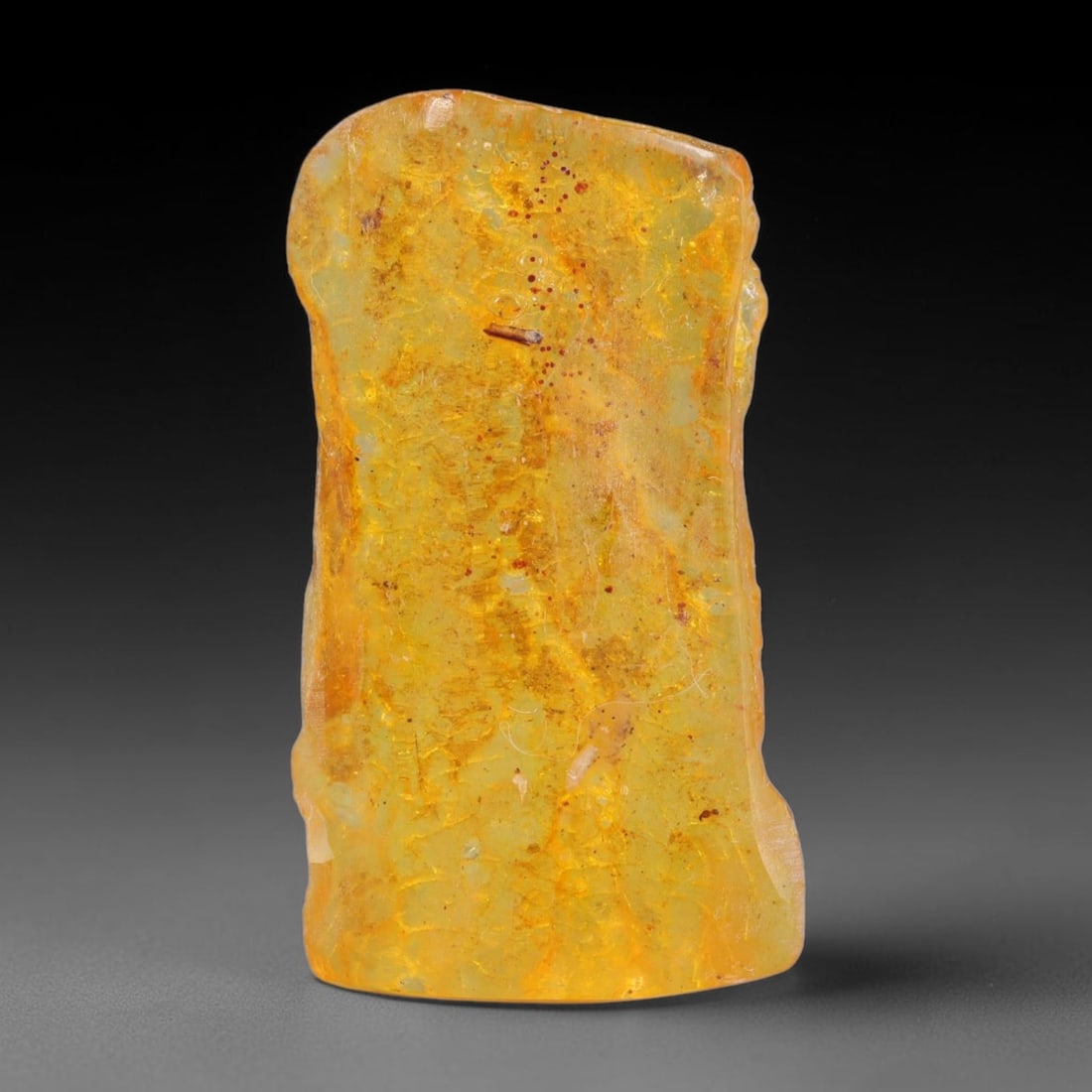 11ct Natural Baltic Polished Loose Freeform Amber Gemstone, 27AT: This smoothly polished freeform amber piece carries warm translucent organic clarity with fine natural fossil flecks and tiny mineral inclusions suspended throughout its 32x18mm flowing unstructured s