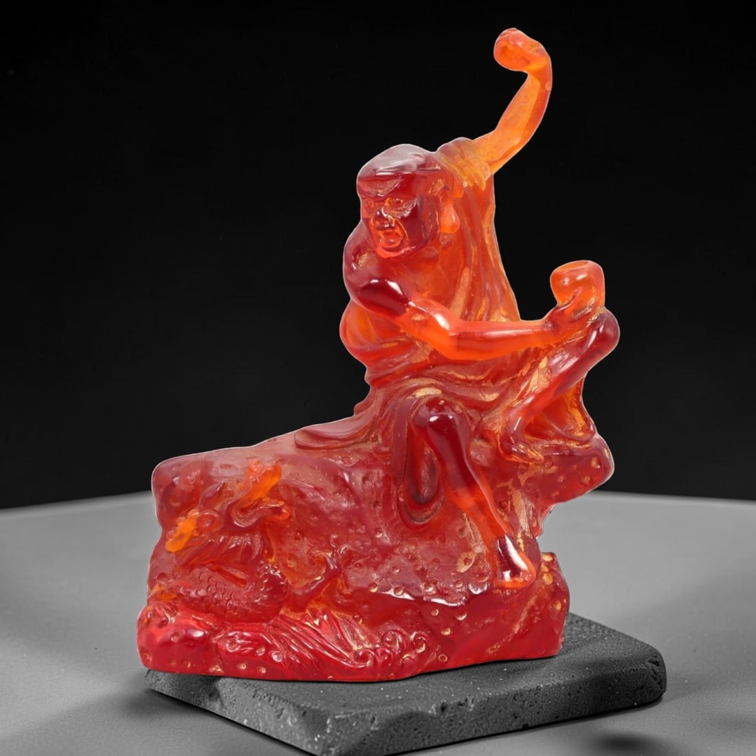 A Chinese Amber-Resin Figure of a Luohan, 34FH: Cast or carved from translucent amber-colored red resin with internal tonal variation, scattered inclusions, and small entrapped bubbles, the figure represents a luohan shown seated in a dynamic postu