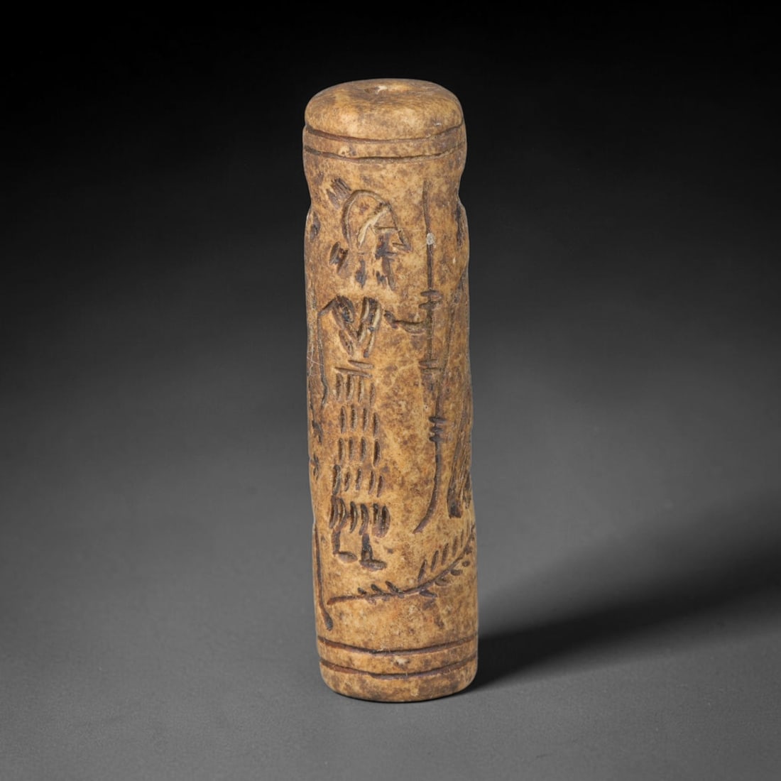 Ancient Mesopotamian Stone Cylinder Seal (c.2300-539 BCE), 65EF: This carved pale weathered stone cylinder seal originates from Ancient Mesopotamia. The cylindrical body features continuous incised imagery encircling the surface, framed by simple horizontal border 