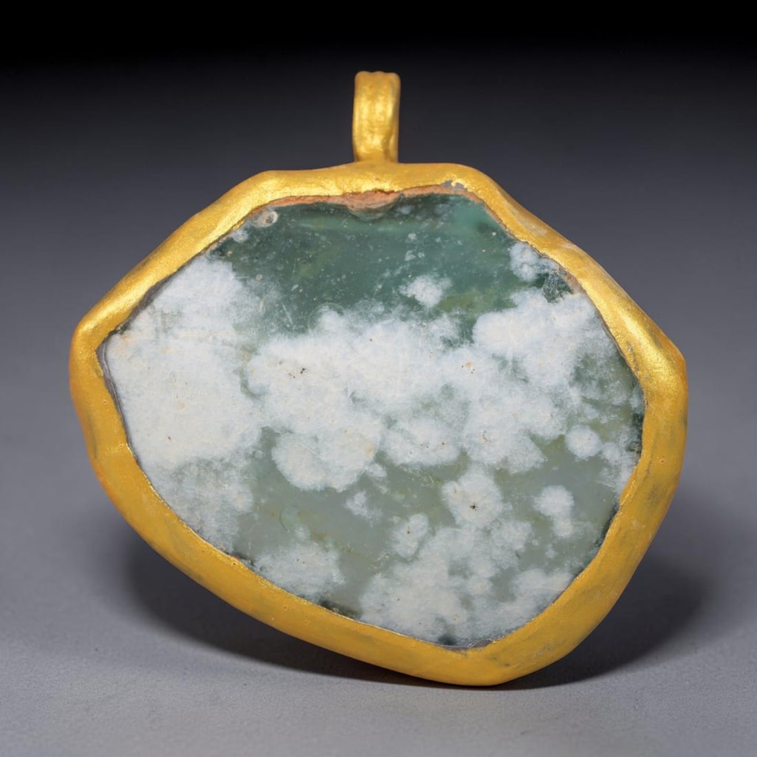 Ancient Roman Glass Slag in Modern Gilt-Edge Pendant, 27EH: This contemporary pendant is crafted from ancient Roman glass slag, featuring a fragmented, iridescent glass surface with weathered patina. The irregular form is bordered by a subtle gilt frame, added