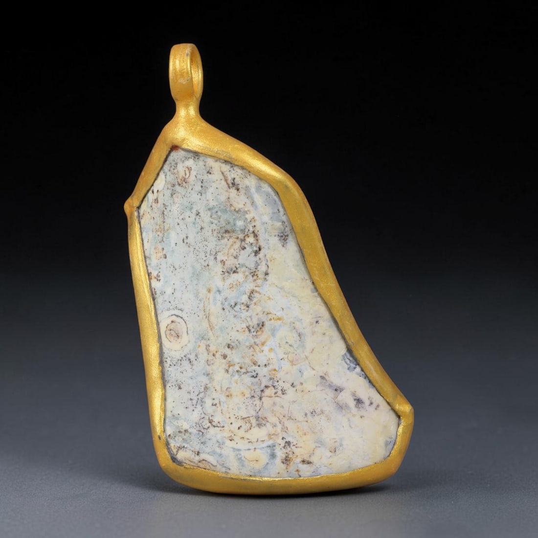 Ancient Roman Glass Slag in Modern Gilt-Edge Pendant, 26EH: This contemporary pendant is crafted from ancient Roman glass slag, featuring a fragmented, iridescent glass surface with weathered patina. The irregular form is bordered by a subtle gilt frame, added