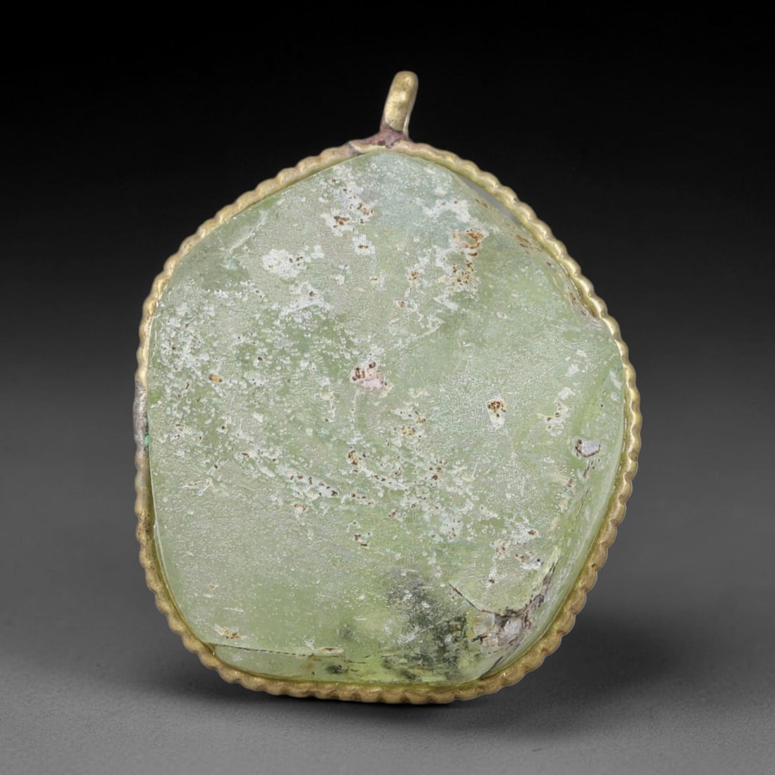 Ancient Roman Glass Slag in Modern Gilt-Edge Pendant, 33EH: This contemporary pendant is crafted from ancient Roman glass slag, featuring a fragmented, iridescent glass surface with weathered patina. The irregular form is bordered by a subtle gilt frame, added