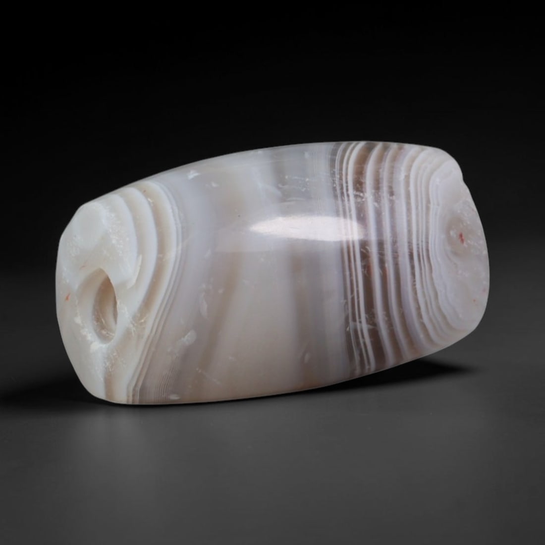 Ancient Assyrian Civilization Banded Agate Barrel Bead (2500-609 BCE), 18AD: This antique banded agate barrel bead originates from the Assyrian Civilization, a Northern Mesopotamian culture renowned for large-scale agate bead carving crafted for palace adornment and elite fune