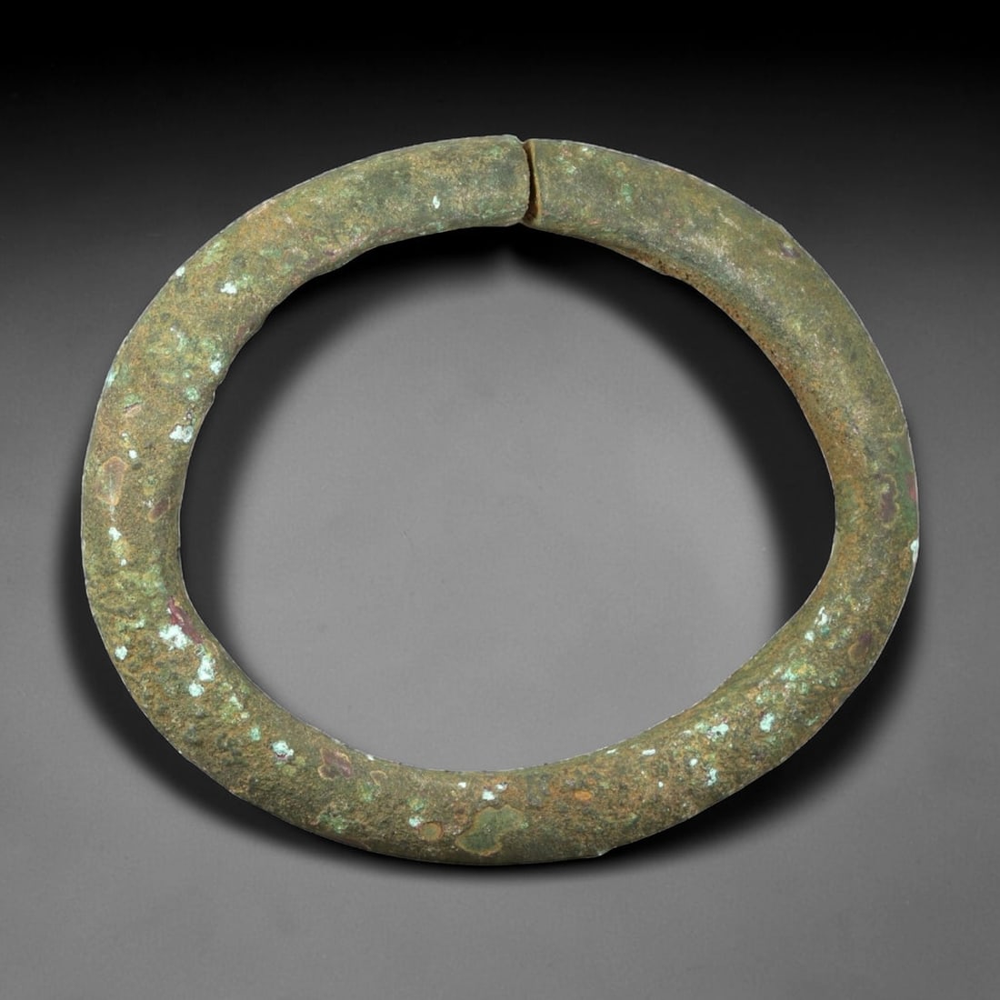 Ancient Bronze Bracelet - Roman Split Bangle, 39BN: A near-continuous bracelet crafted from cast bronze, with a rounded cross-section and a small opening at the top. The simple form is characteristic of utilitarian Roman provincial jewelry, designed fo