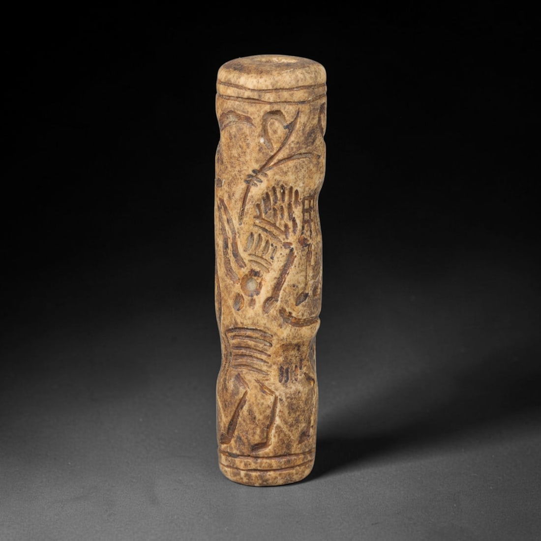 Ancient Mesopotamian Stone Cylinder Seal (c.2300-539 BCE), 70EF: This carved pale weathered stone cylinder seal originates from Ancient Mesopotamia. The cylindrical body features continuous incised imagery encircling the surface, framed by simple horizontal border 
