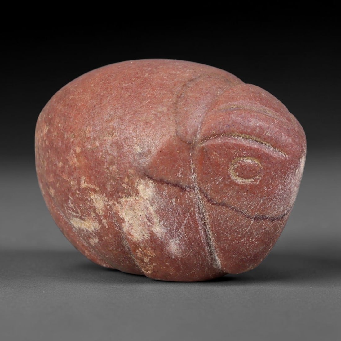 Ancient Medieval Seljuk Red Stone Zoomorphic Talisman Amulet (11th-13th Centuries CE), 42EF: This compact zoomorphic amulet is carved from rich red stone, originating from the medieval Seljuk realm. The form features minimal stylised incised lines defining facial features and segmented contou