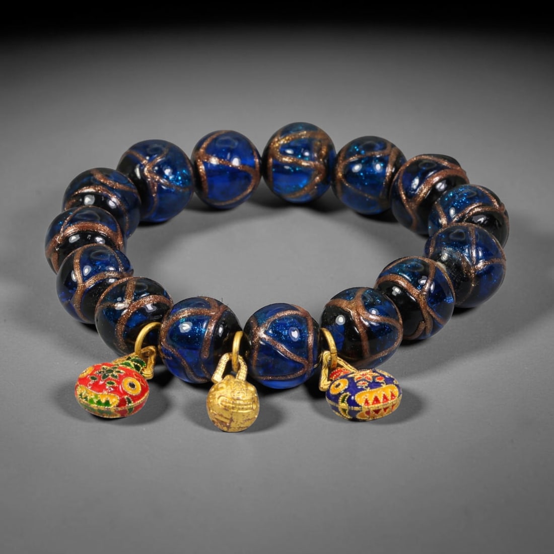 A Chinese Glass Beaded Bracelet - Blue Gold Sand Glass Charm Strand, 10AP: Hand-strand bracelet composed of round 14mm hand-blown Chinese glass beads, each crafted with translucent deep blue glass infused with fine gold aventurine sand, detailed with hand-painted bronze tone