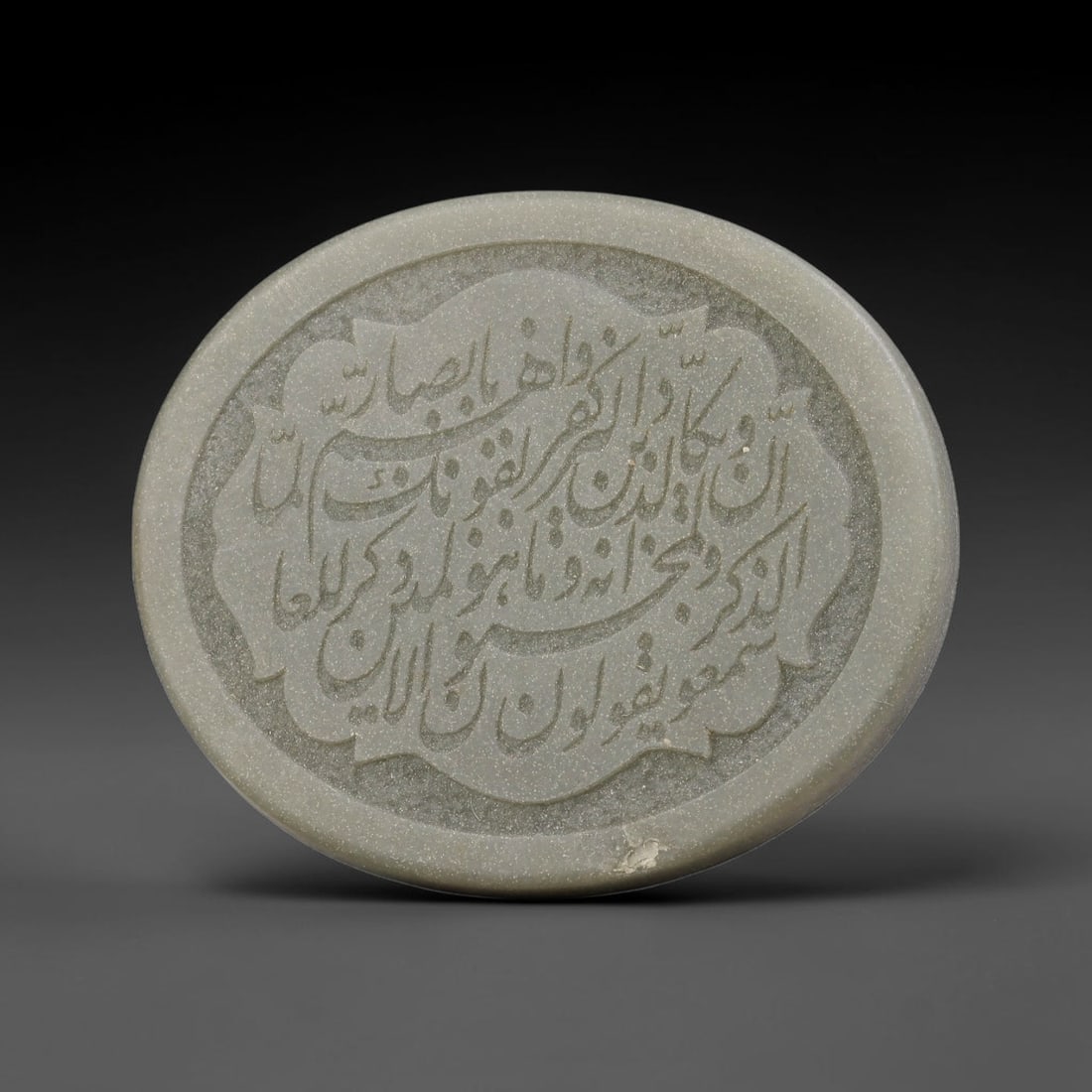An Islamic Natural Green Stone Circular Script Engraved Talisman Tablet, 40FG: This polished green stone talisman tablet with elaborate concentric layered script engraving covering the central face, framed within a stylized petal-shaped inner border. Fine recessed engraved detai