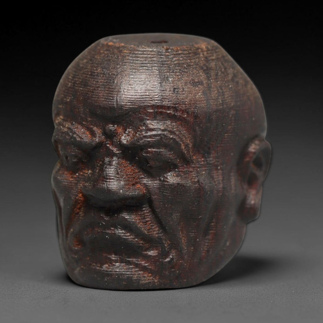 A Chinese Agar Wood Carved Head Art Bead, 37BX: Chinese agar wood head-form art bead measuring 22 x 20 mm. Detailed sculpted facial features cover the exterior surface, with a continuous central bore designed for stringing within beaded strands. Th