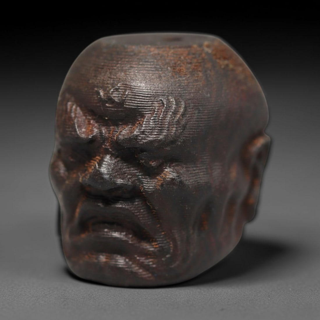 A Chinese Agar Wood Carved Head Art Bead, 31BX: Chinese agar wood head-form art bead measuring 22 x 20 mm. Detailed sculpted facial features cover the exterior surface, with a continuous central bore designed for stringing within beaded strands. Th