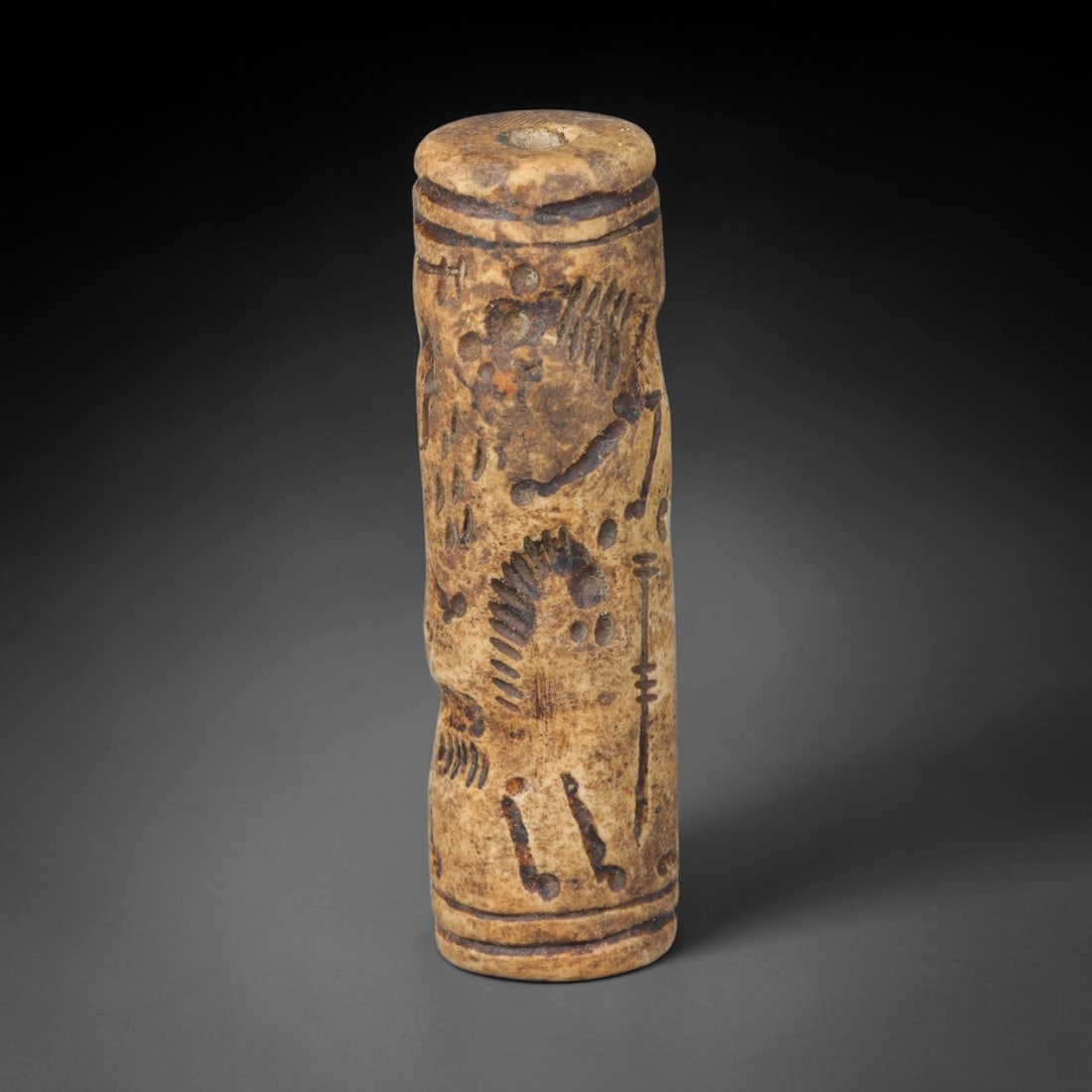 Ancient Mesopotamian Stone Cylinder Seal (c.2300-539 BCE), 62EF: This carved pale weathered stone cylinder seal originates from Ancient Mesopotamia. The cylindrical body features continuous incised imagery encircling the surface, framed by simple horizontal border 