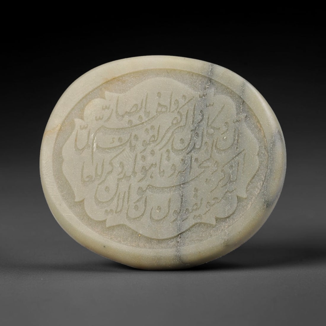 An Islamic Natural Green Stone Circular Script Engraved Talisman Tablet, 41FG: This polished green stone talisman tablet with elaborate concentric layered script engraving covering the central face, framed within a stylized petal-shaped inner border. Fine recessed engraved detai