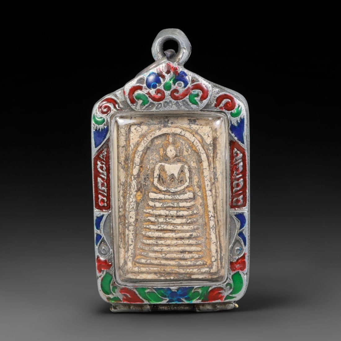 Thai Buddhist Folk Tradition Enclosed Amulet Pendant with Decorative Metal Casing, 19AH: This Thai sacred amulet is housed within an ornate hinged metal protective casing fitted with a top loop for wear as a pendant. The casing features intricate embossed surface detailing and a continuou