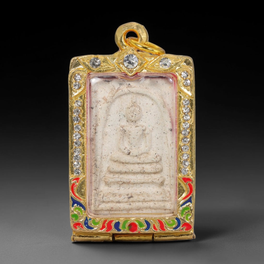 Thai Buddhist Folk Tradition Enclosed Amulet Pendant with Decorative Metal Casing, 12AH: This Thai sacred amulet is housed within an ornate hinged metal protective casing fitted with a top loop for wear as a pendant. The casing features intricate embossed surface detailing and a continuou