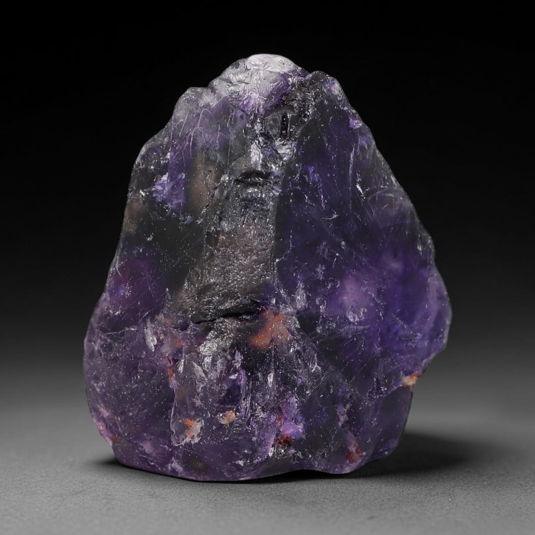 165ct Natural Chinese Deep Violet Purple Fluorite Rough, 8AT: This rugged fluorite rough boasts rich layered violet purple saturation blended with warm rust-colored mineral inclusions that streak its uneven raw surface, soft translucency lets light drift through