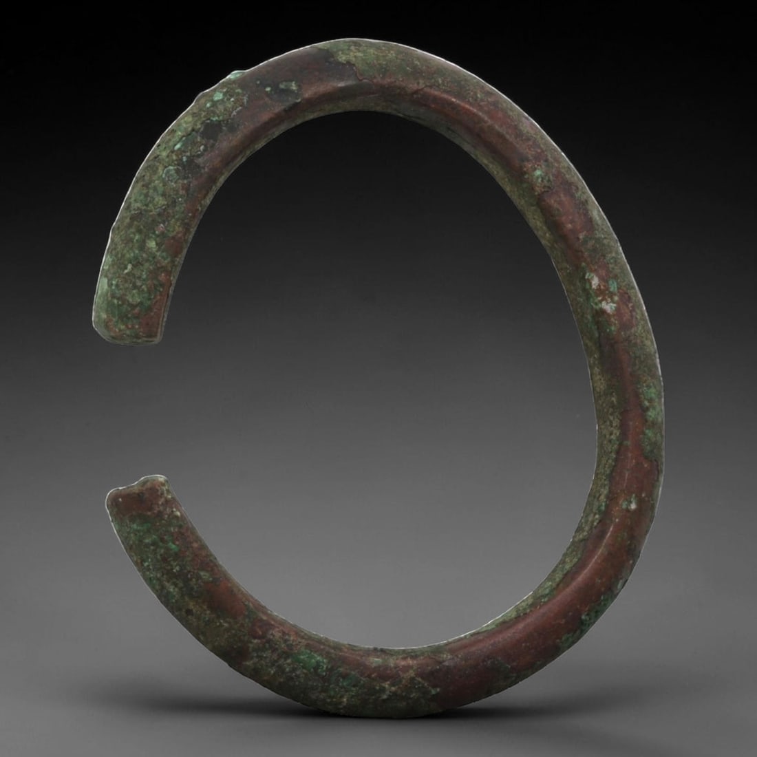 Ancient Bronze Bracelet - Roman Penannular Bangle, 26BN: A penannular bronze bracelet of ancient Roman origin, formed from a thick, rounded bronze band with a robust profile. The open terminals are plain, with subtle signs of shaping typical of Roman provin