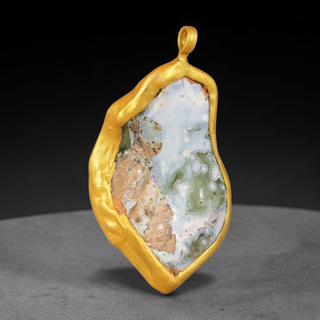 Ancient Roman Glass Slag in Modern Gilt-Edge Pendant, 67FY: This contemporary pendant is crafted from ancient Roman glass slag, featuring a fragmented, iridescent glass surface with weathered patina. The irregular form is bordered by a subtle gilt frame, added