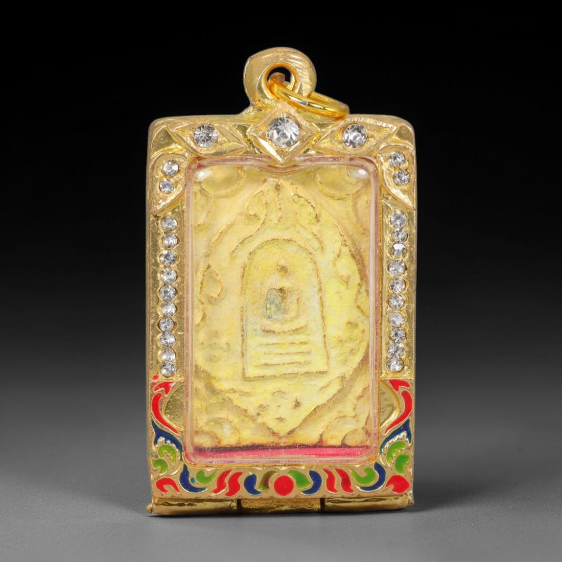 Thai Buddhist Folk Tradition Enclosed Amulet Pendant with Decorative Metal Casing, 5AH: This Thai sacred amulet is housed within an ornate hinged metal protective casing fitted with a top loop for wear as a pendant. The casing features intricate embossed surface detailing and a continuou