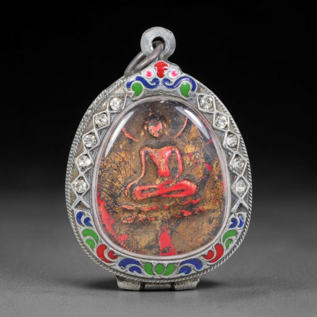 Thai Buddhist Folk Tradition Enclosed Amulet Pendant with Decorative Metal Casing, 36AH: This Thai sacred amulet is housed within an ornate hinged metal protective casing fitted with a top loop for wear as a pendant. The casing features intricate embossed surface detailing and a continuou