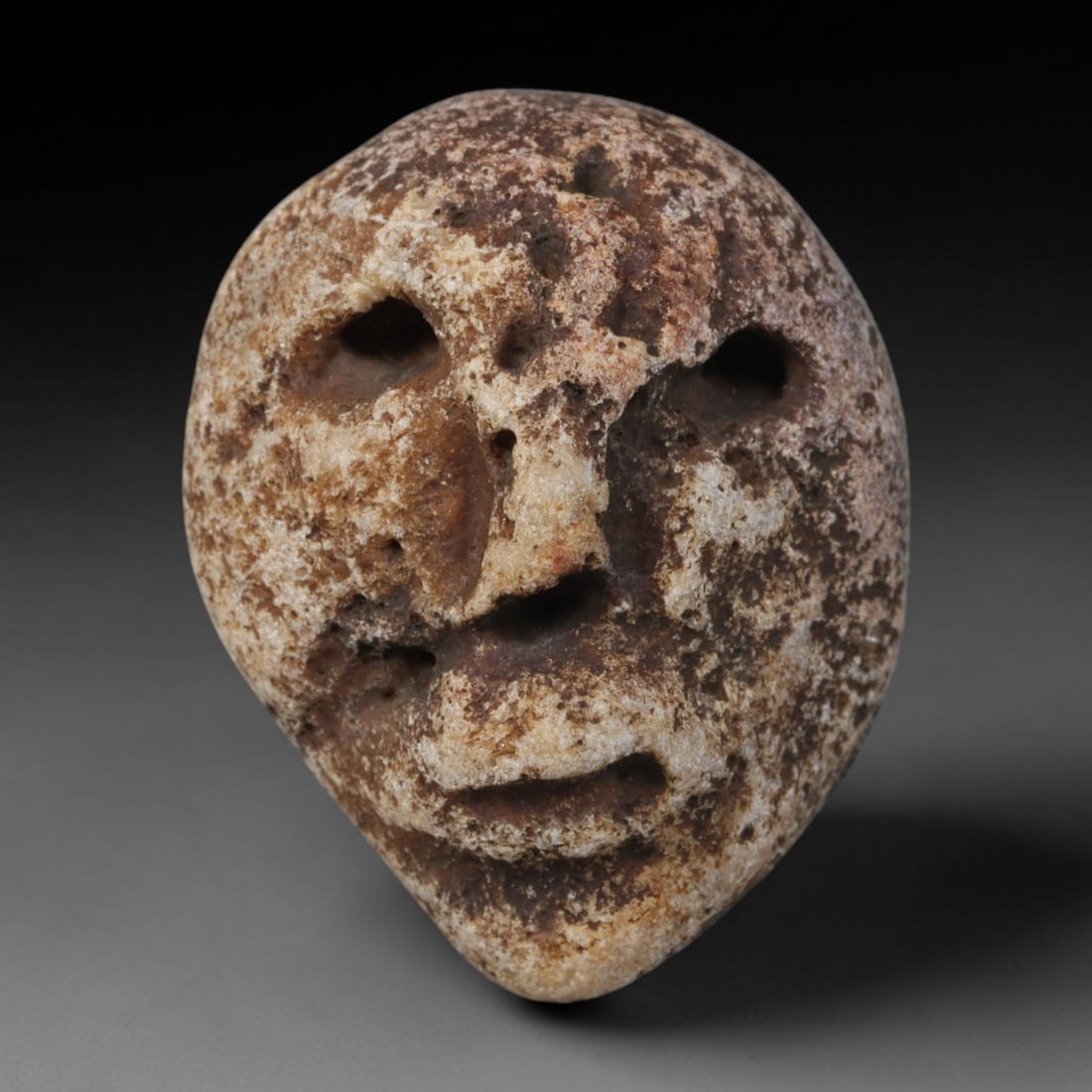 Ancient Medieval Mediterranean Hand Carved Stone Maskette Amulet, 56AP: Miniature wearable sacred talisman hand hewn from natural soft stone, originating from Medieval Mediterranean cultural craft traditions. Small carved stone amulets were widespread personal artifacts a