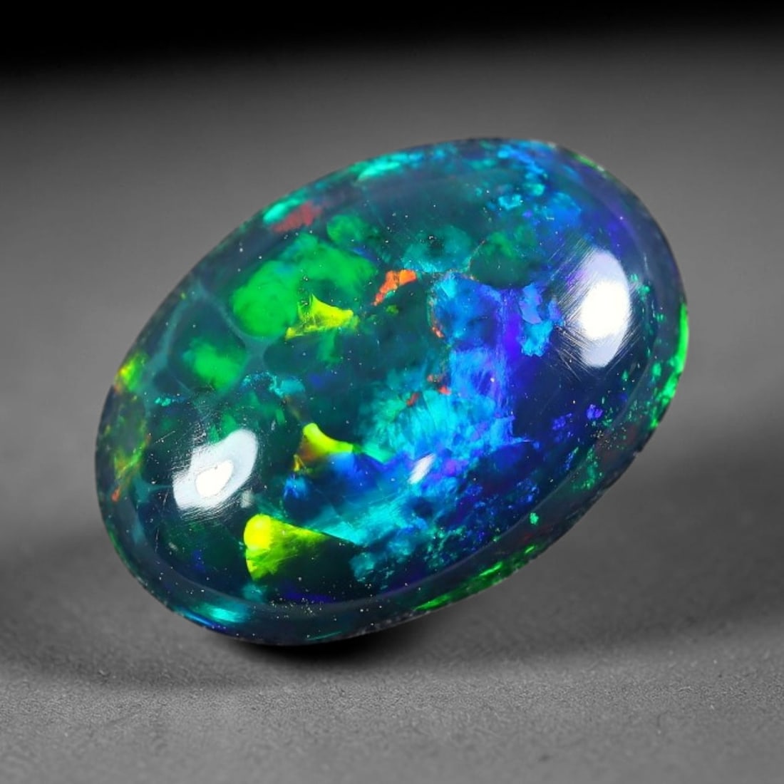 1.70ct Natural Ethiopian Welo Black Smoked Opal Cabochon Loose Gemstone, 14FX: This fully polished Ethiopian Welo opal features a dark smoked base with vivid, sweeping play-of-color shifting across its glossy dome surface, measured at 11x8x3mm. The black smoke treatment deepens 