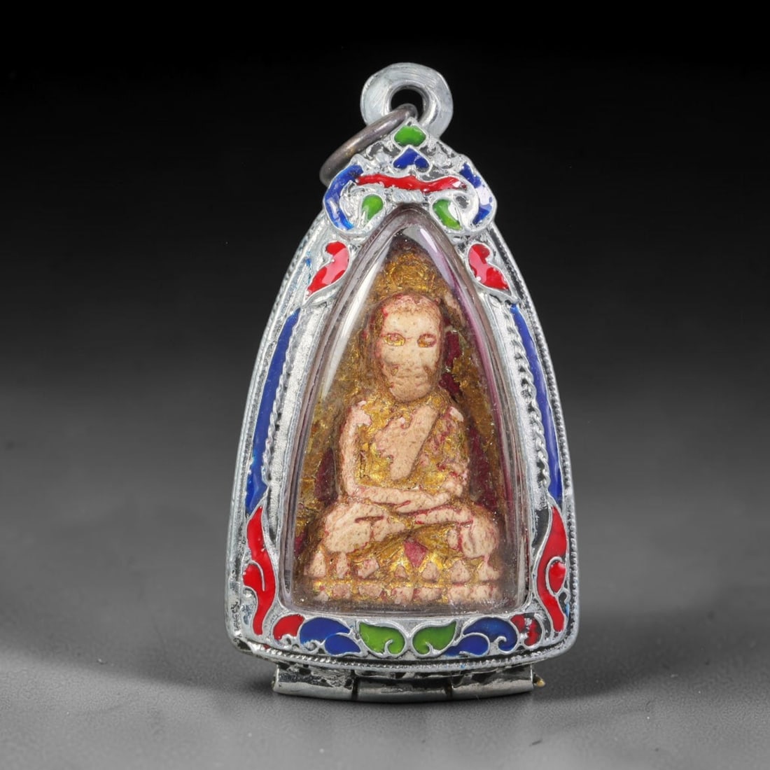Thai Buddhist Folk Tradition Enclosed Amulet Pendant with Decorative Metal Casing, 35AH: This Thai sacred amulet is housed within an ornate hinged metal protective casing fitted with a top loop for wear as a pendant. The casing features intricate embossed surface detailing and a continuou
