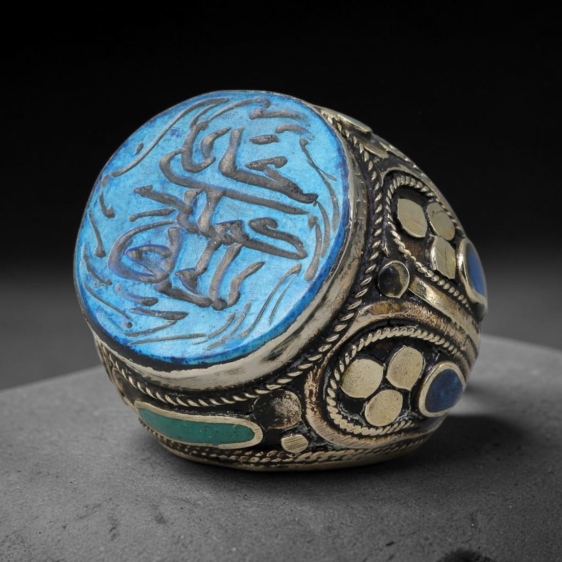 Vintage Islamic Handcrafted Silver Plated Calligraphic Talisman Statement Ring, 20BX: This vintage hand-wrought Islamic statement ring features a central engraved panel bearing traditional calligraphic detailing, set within an ornate silver-plated metal band. The mounting is enriched w