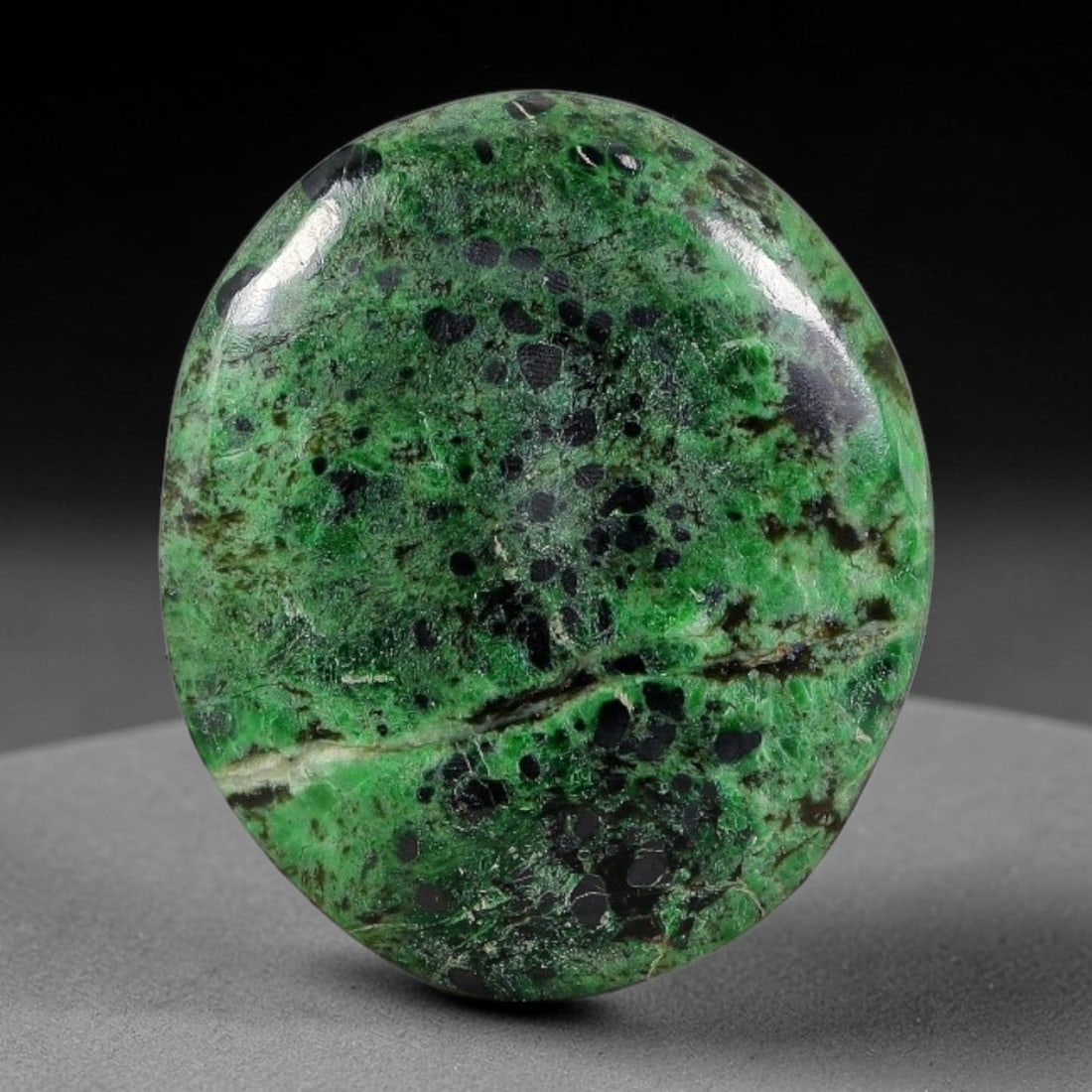 12.78ct Natural Burmese Type A Black Dot Spotted Green Jadeite Jade Cabochon, 44FA: This single untreated natural Burmese Type A oval jadeite jade cabochon weighs 12.78ct, measuring 19.6x16.8x4.4mm. The bright emerald green matrix is densely dotted with round black mineral spots, int