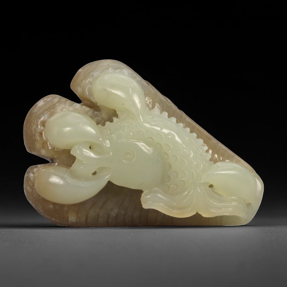 Natural XinJiang Hetian Nephrite Jade Claw with Fish Carving, 1FB: Carved from bi-colored jade with a creamy pale green body contrasted by a warm brown outer skin, the object is worked in the round as a stylized claw grasping a fish. The claw is rendered with three c
