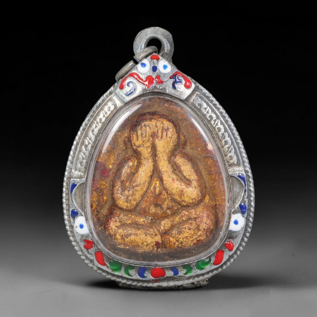 Thai Buddhist Folk Tradition Enclosed Amulet Pendant with Decorative Metal Casing, 40AH: This Thai sacred amulet is housed within an ornate hinged metal protective casing fitted with a top loop for wear as a pendant. The casing features intricate embossed surface detailing and a continuou