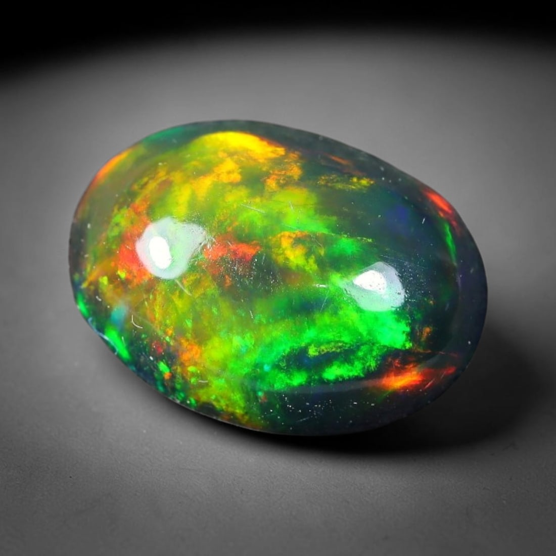 1.93ct Natural Ethiopian Welo Black Smoked Opal Cabochon Loose Gemstone, 11FX: This fully polished Ethiopian Welo opal features a dark smoked base with vivid, sweeping play-of-color shifting across its glossy dome surface, measured at 11x8x4mm. The black smoke treatment deepens 