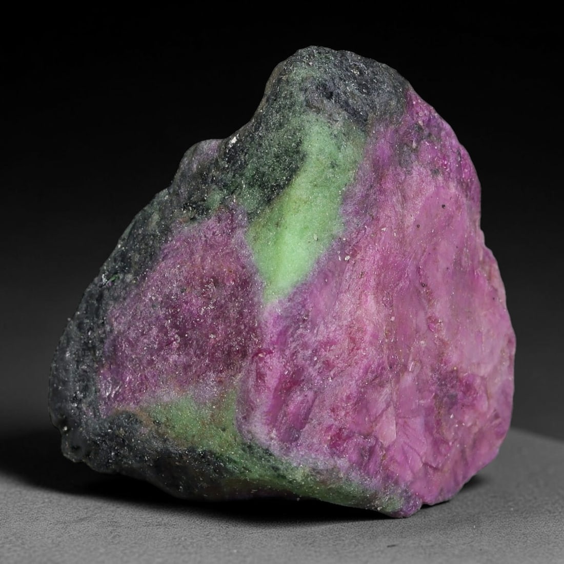 114ct Natural Tanzanian Ruby Zoisite Raw Rough Specimen Mineral Stone, 95FB: This unpolished mineral rough is natural ruby zoisite sourced from Tanzania, exhibiting distinct banded mineral segregation of vibrant green zoisite, magenta ruby crystals, and dark hornblende inclusi