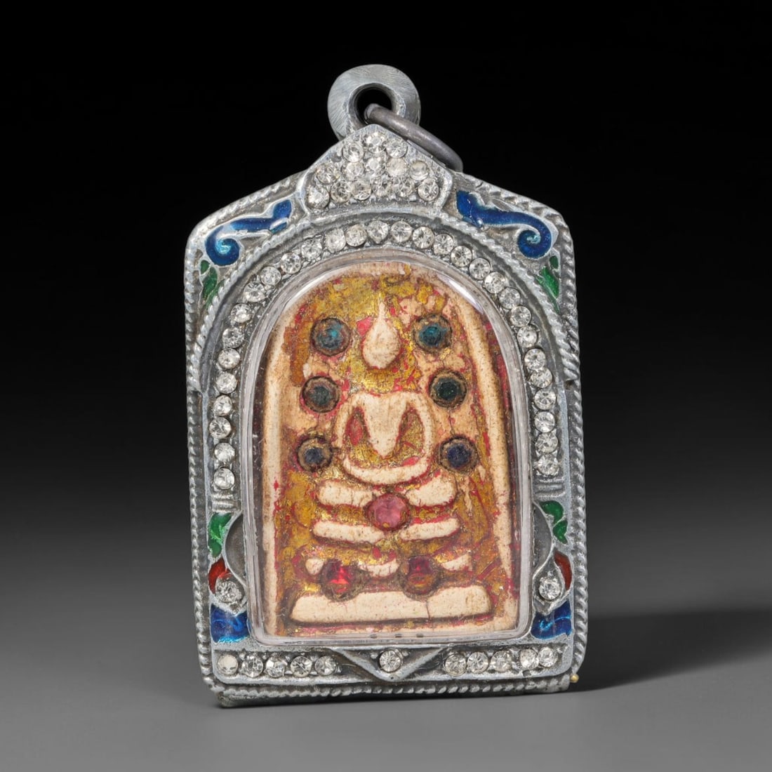 Thai Buddhist Folk Tradition Enclosed Amulet Pendant with Decorative Metal Casing, 37AH: This Thai sacred amulet is housed within an ornate hinged metal protective casing fitted with a top loop for wear as a pendant. The casing features intricate embossed surface detailing and a continuou