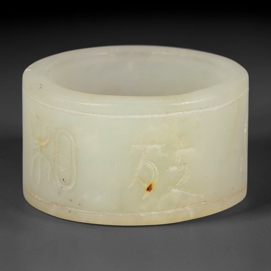 A Chinese Nephrite Jade Cylinder Inscribed Character Ornament, 9AE: Formed from pale celadon nephrite jade marked by faint mineral speckles and a small russet inclusion on the outer wall, this hollow short cylindrical stone form bears finely hand-incised Chinese calli