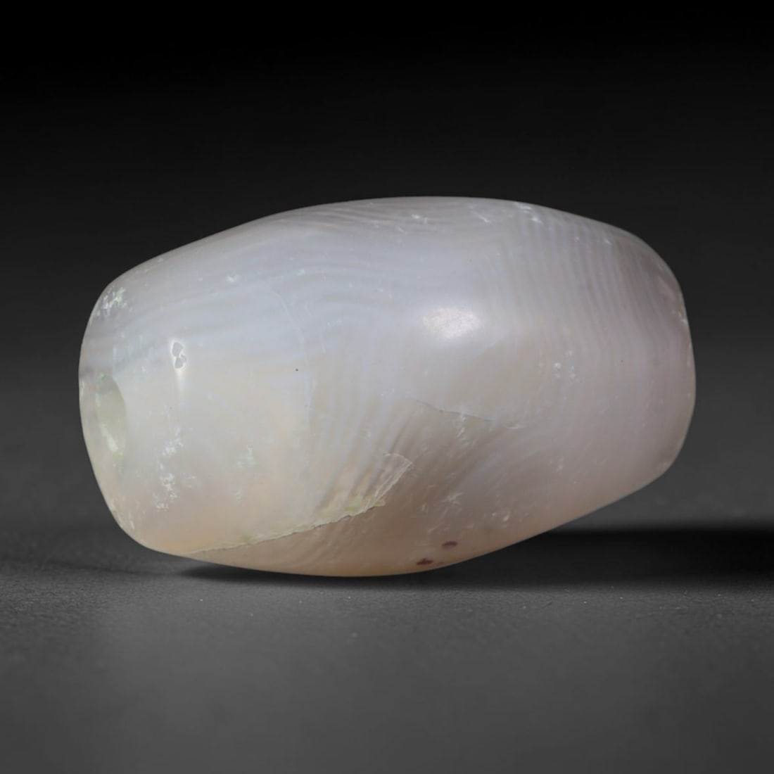 Ancient Kushan Empire Striated Pale Blush Banded Agate Barrel Bead (30 CE - 375 CE), 67AD: This soft translucent banded agate barrel bead originates from the Kushan Empire, a pivotal Central Asian power that unified Indo-Silk Road trade and fused Hellenistic, Indian and steppe lapidary trad