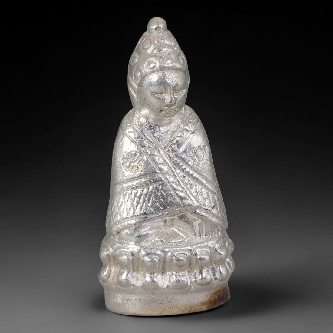 Thai Silvered Metal Sacred Miniature Figurine Amulet, 3AH: Small solid cast metal sacred statuette finished with silvered surface detailing, fully sculpted with layered relief ornamentation across the robe, head adornment and tiered base form. Subtle natural 