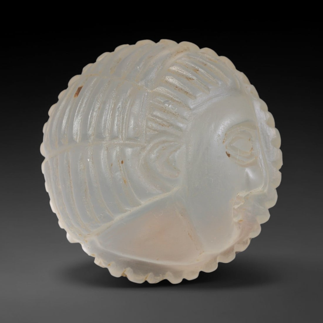 Ancient Medieval Early Islamic Period Glass Cameo Bead (c.632-1050 CE), 51EF: This translucent pale glass cameo bead originates from the Early Islamic period. The surface features raised relief carving depicting a stylised facial motif with detailed incised hairwork and scallop