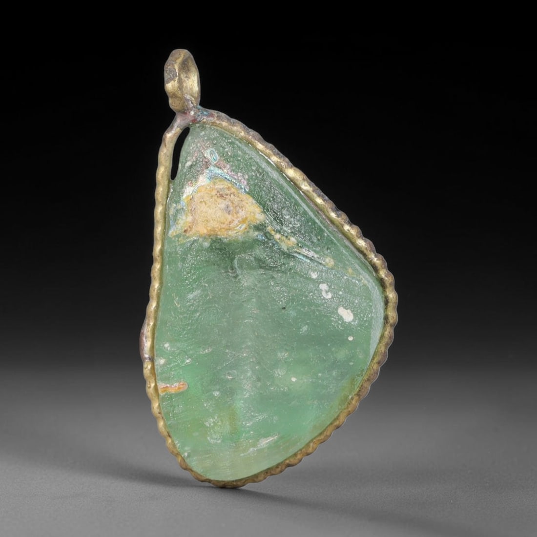 Ancient Roman Glass Slag in Modern Gilt-Edge Pendant, 36EH: This contemporary pendant is crafted from ancient Roman glass slag, featuring a fragmented, iridescent glass surface with weathered patina. The irregular form is bordered by a subtle gilt frame, added