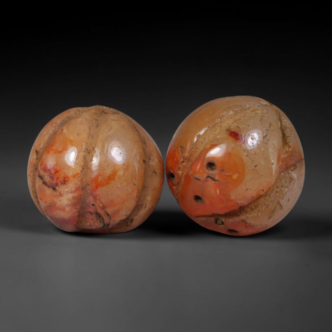 Ancient Medieval Khmer Angkor Culture Carved Carnelian Melon Bead Pair (802-1431 CE), 50AE: This matched pair of antique hand-carved melon form carnelian beads originates from Khmer Angkor Culture, the medieval Southeast Asian civilization renowned for crafting ritual chalcedony adornments f