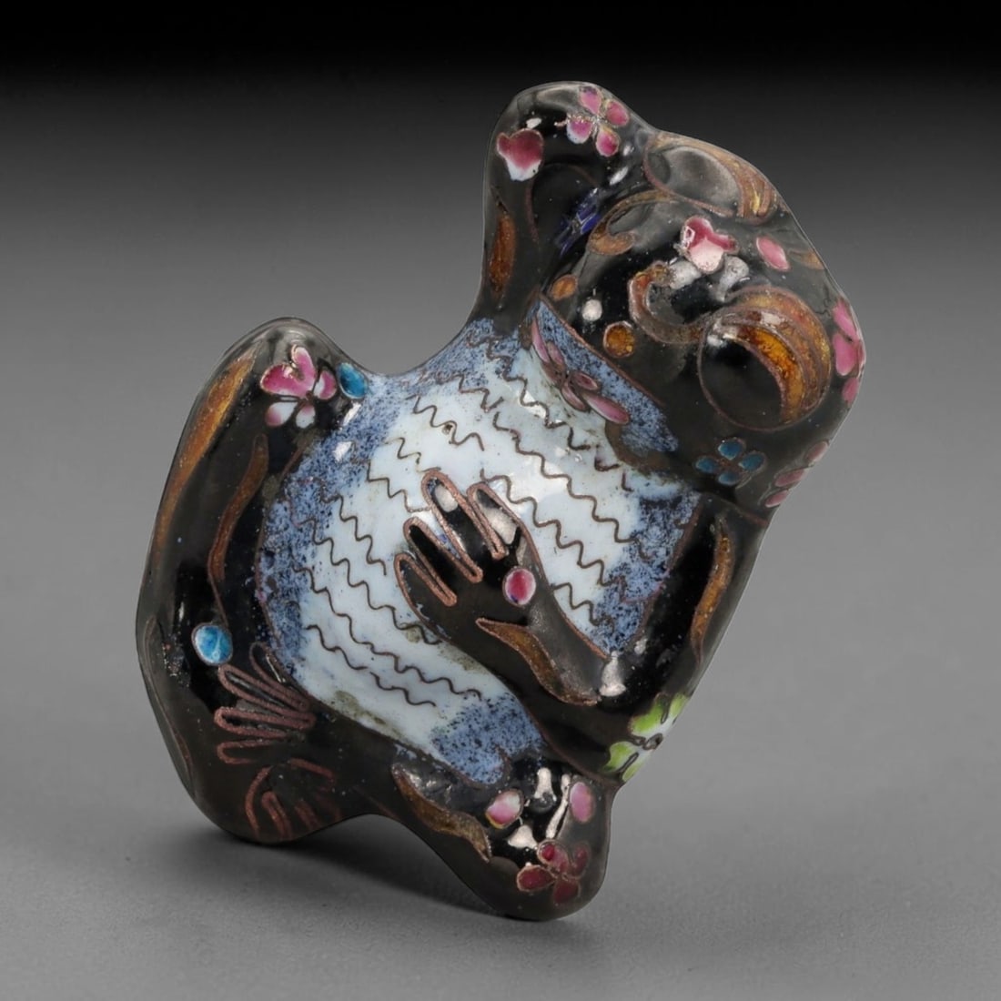 A Chinese Enamel Frog Effigy, 10FH: Modeled as a stylized frog shown seated upright with the head tilted upward and forelimbs drawn toward the chest, the effigy is formed from a metal core and decorated with painted enamel rather than c