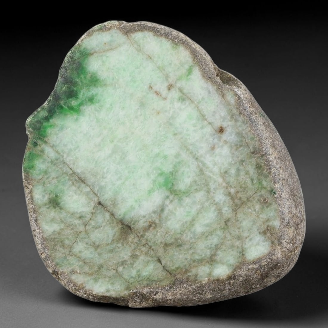 265ct Natural Type A Burmese Side Floating Green Jadeite Jade Sliced Rough, 19FA: This specimen is a natural sliced rough pebble of untreated Type A Burmese jadeite, retaining original dark weathered rocky rind along its full outer perimeter. Its polished cut face displays pale mil