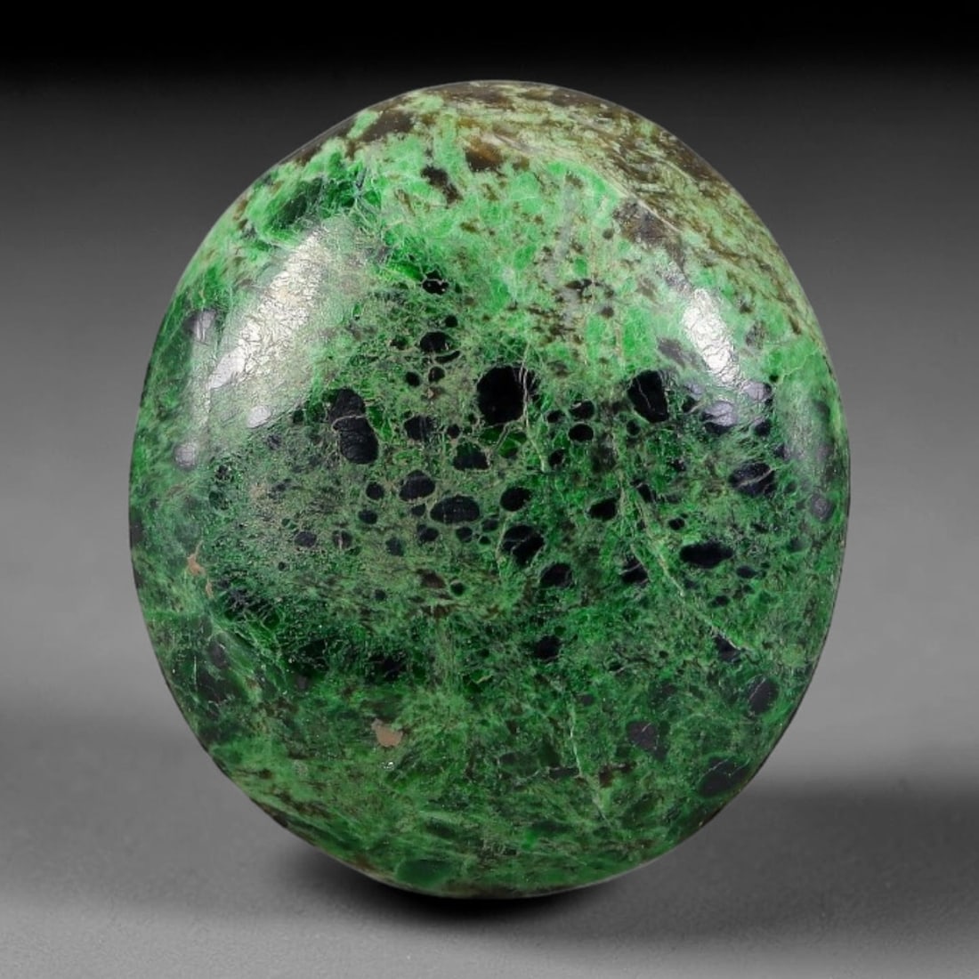 16.15ct Natural Burmese Type A Black Dot Spotted Green Jadeite Jade Cabochon, 39FA: This single untreated natural Burmese Type A oval jadeite jade cabochon weighs 16.15ct, with dimensions of 21x18.5x5mm. The bright emerald green body is densely covered with round black mineral inclus