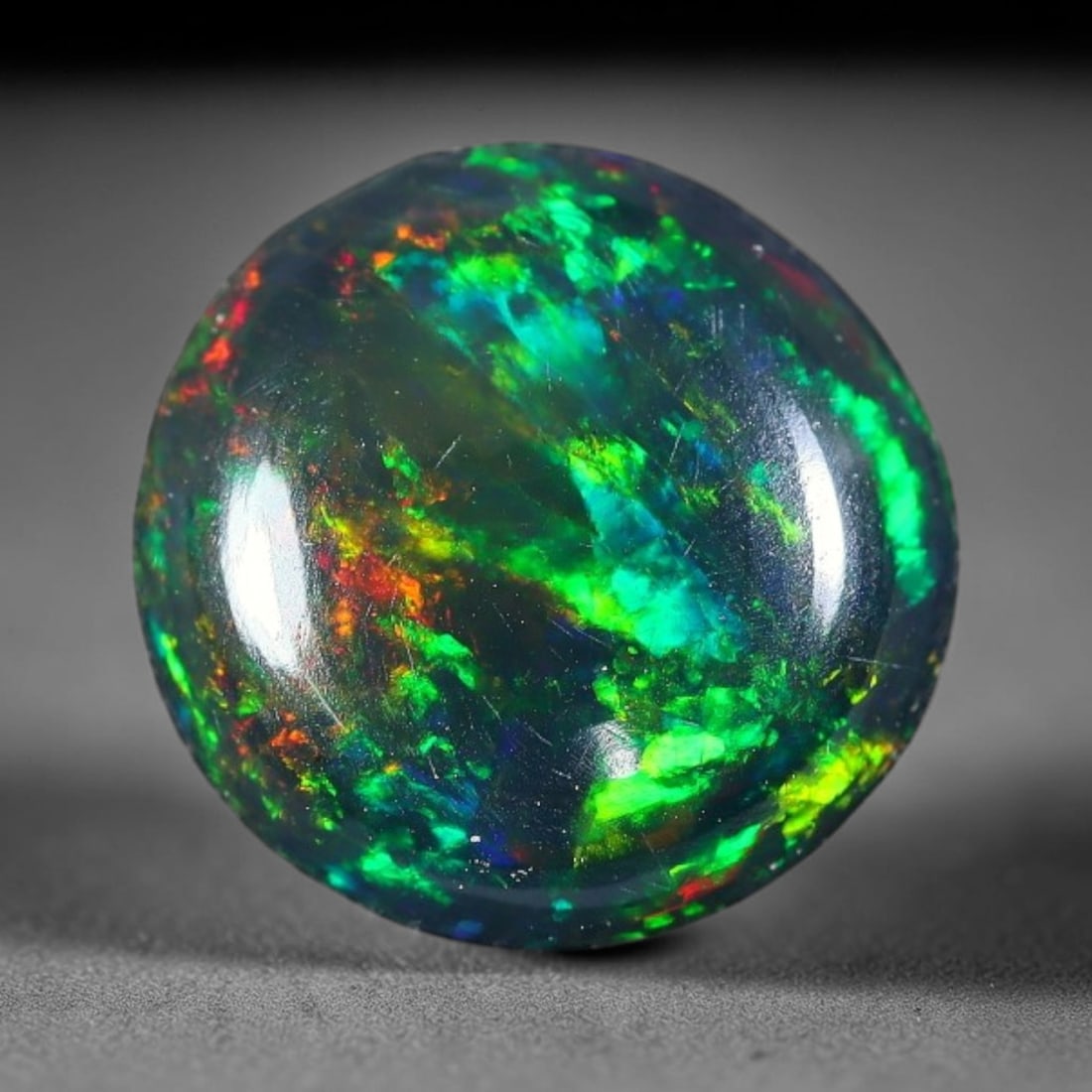 1.47ct Natural Ethiopian Welo Black Smoked Opal Cabochon Loose Gemstone, 24FX: This fully polished Ethiopian Welo opal features a dark smoked base with vivid, sweeping play-of-color shifting across its glossy dome surface, measured at 9x3mm. The black smoke treatment deepens the