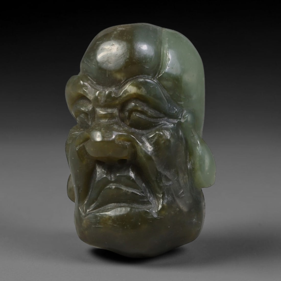 Natural Vintage Chinese Nephrite Jade Dark Mixed Green Arhat Head Carved Face Bead, 25AP: Hand-carved vintage Chinese strung bead crafted from natural vintage Chinese nephrite jade, measuring 3cm x 1.8cm. This barrel-shaped bead is intricately sculpted into a solemn Buddhist Arhat head, fe