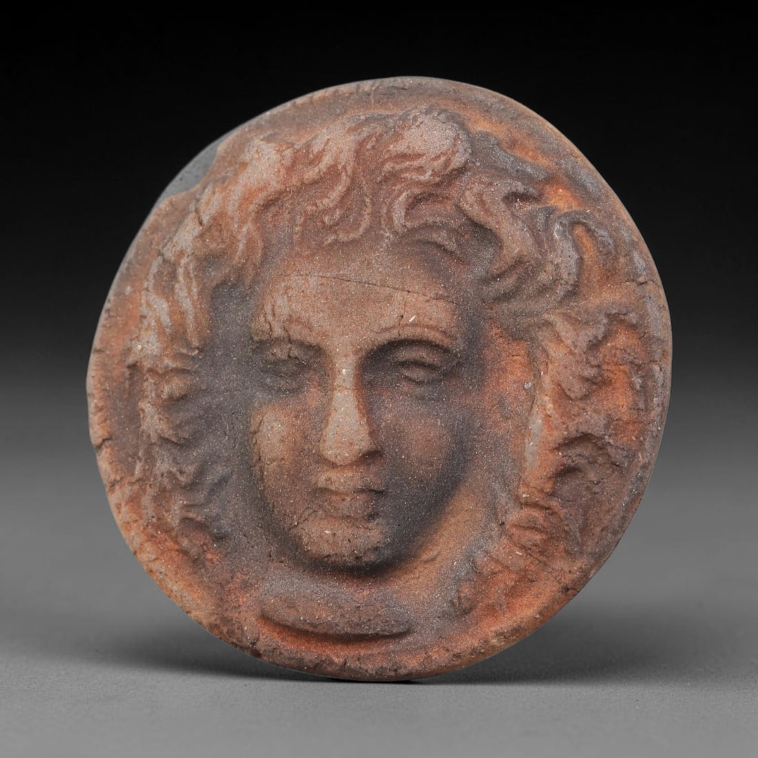 Ancient Hellenistic Terracotta Cameo Stamp (323-31 BCE), 38EK: This ancient mould-formed terracotta cameo stamp originates from the Hellenistic cultural sphere, crafted as a wearable seal amulet with an integral conical perforated reverse for suspension. The obve