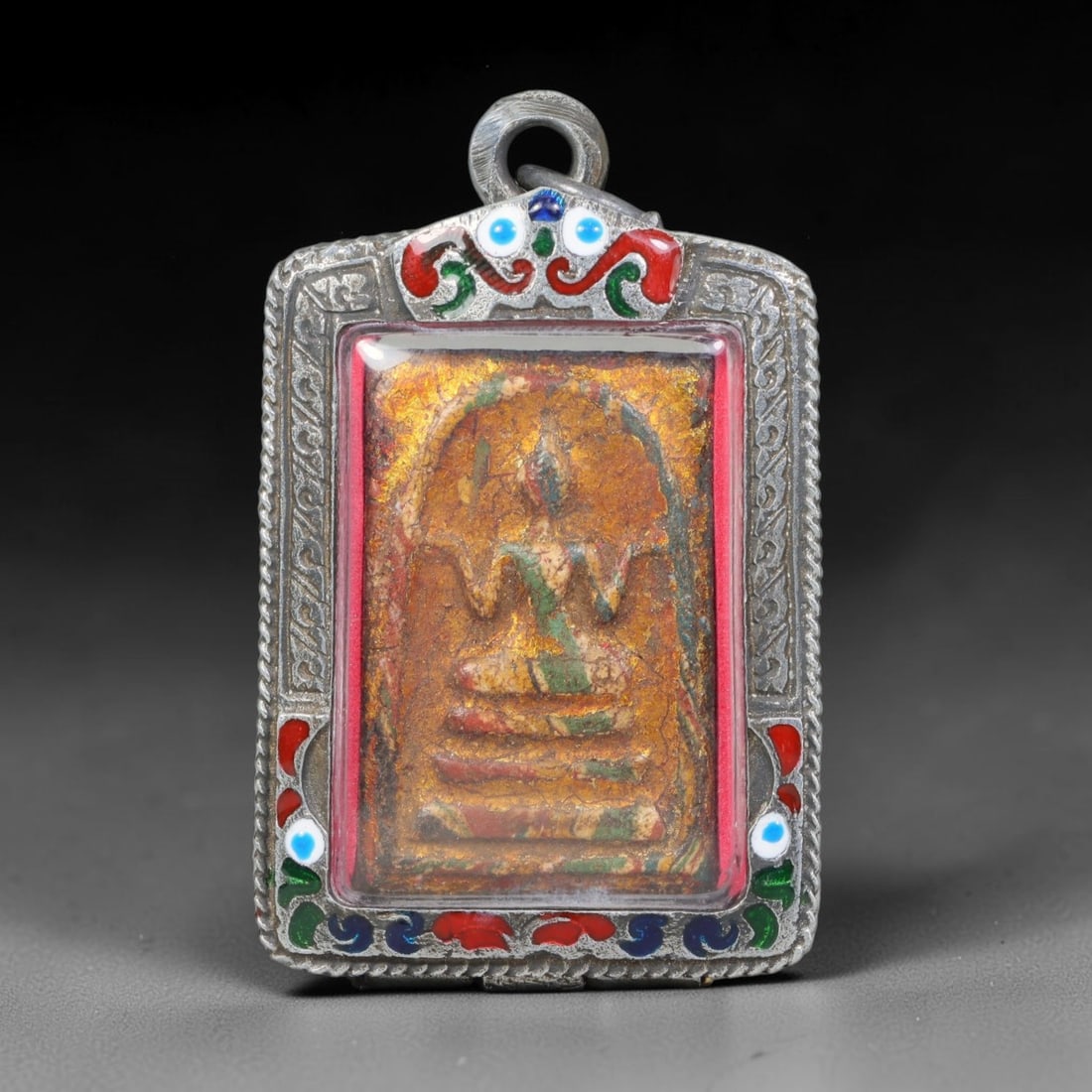 Thai Buddhist Folk Tradition Enclosed Amulet Pendant with Decorative Metal Casing, 42AH: This Thai sacred amulet is housed within an ornate hinged metal protective casing fitted with a top loop for wear as a pendant. The casing features intricate embossed surface detailing and a continuou
